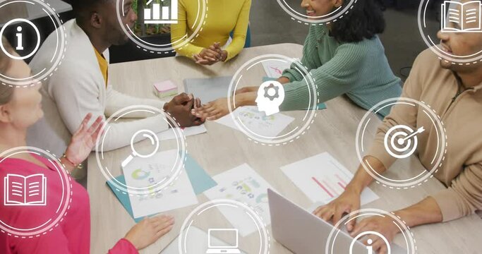 Animation of digital icons over team of diverse colleagues stacking their hands together at office