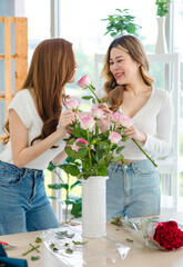 Asian professional successful female florist designer flower shop owner entrepreneur and colleague employee helping decorating pink roses bouquet in white ceramic vase in floral garden store studio