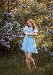 girl in a blue dress with a hat in the park near lilac shrub
