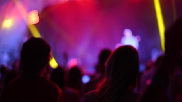 Blurred silhouettes of people raise hands in front of colorful lights in concert