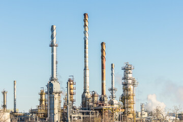 Spiral Topped Spires. Oil refinery in cold blue winter. Tall steam towers and cooling smoke stacks, a facility for receiving and processing oil and fossil fuels