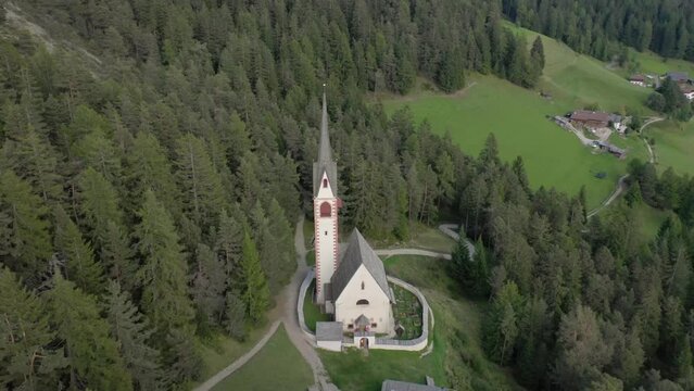 Aerial drone view of an old secluded mountain top church in the Italian alps surrounded by a forrest of trees 04