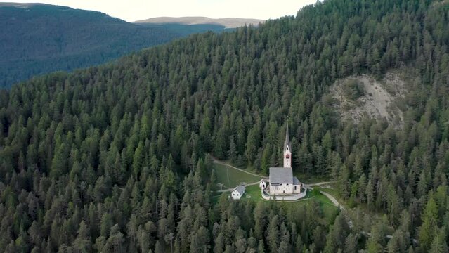 Aerial drone view of an old secluded mountain top church in the Italian alps surrounded by a forrest of trees 03