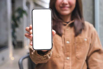 Mockup image of a young woman holding and showing a mobile phone with blank white screen