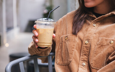 Closeup image of a young woman holding and drinking iced coffee in cafe