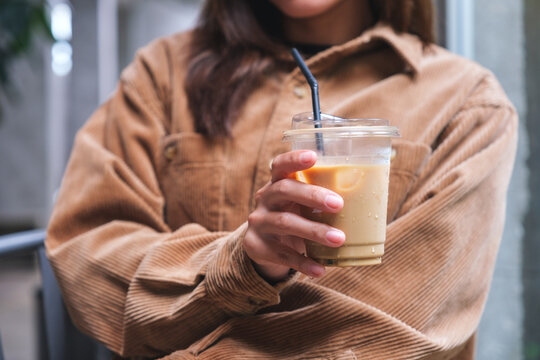 Closeup image of a young woman holding and drinking iced coffee in cafe