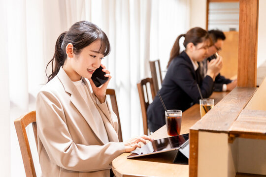 カフェのカウンターでスマホを使って通話するスーツを着たアジア人のビジネスウーマン
