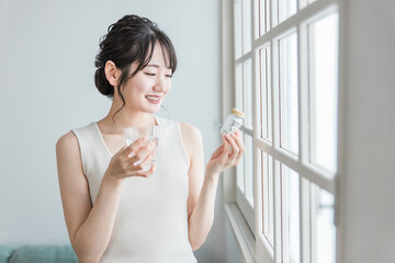 薬・サプリメント・ビタミン剤・整腸剤を飲む若いアジア人女性
