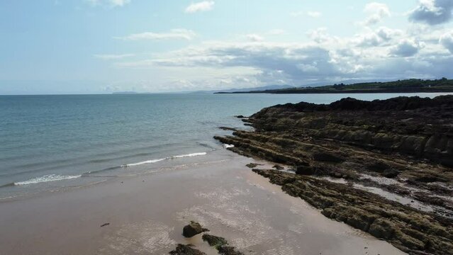 Aerial view Traeth Lligwy Jurassic rocky weathered rugged Anglesey shoreline, pull back shot