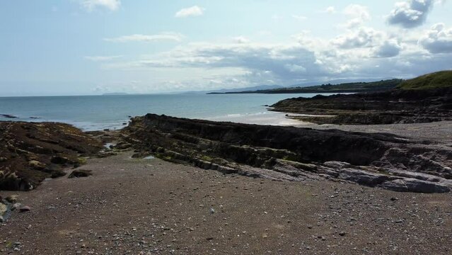 Aerial view Traeth Lligwy Jurassic rocky weathered rugged Anglesey coastal shoreline, low dolly right