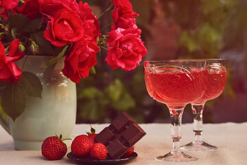 Aesthetic summer table settings. Couple glasses of red strawberry wine, strawberry and chocolate. Roses bouquet.