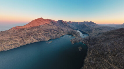 A breathtaking aerial panorama of the Cuillin Mountains at sunrise, showcasing Loch Coruisk and Sgurr na Stri.