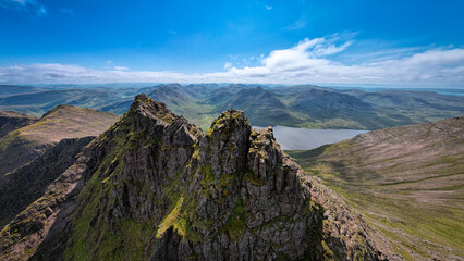 Breathtaking aerial view of a man standing on top of An Teallach mountain on a clear summer day in Scotland revealing the great wilderness.