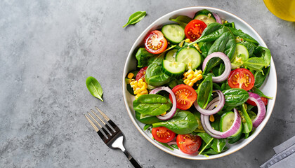 Spring vegan salad with spinach, cherry tomatoes, corn salad, baby spinach, cucumber and red onion. Healthy food concept. Gray stone table. Top view. Copy space