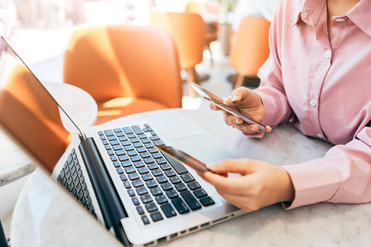 A woman sitting in a café is using her credit card to make online purchases.