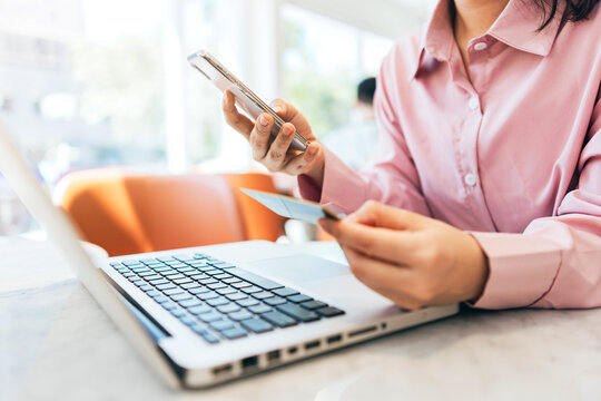A woman sitting in a café is using her credit card to make online purchases.