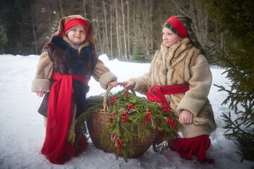 Teen and little girl in thick coat with basket of fir branches and berries in cold winter day in...