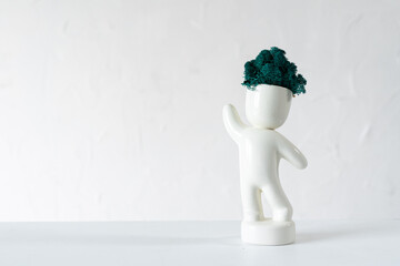 White ceramic figurine of human with colorful stabilized moss from head is standing with hans up. 