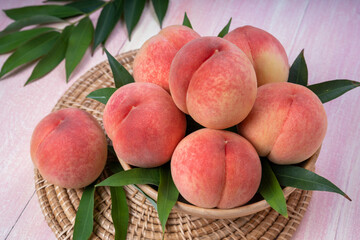 Pink Peach on wooden basket, White Peach with leaf on pink wooden background.