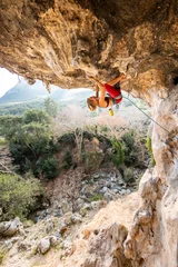 Fotobehang A young rock climber on an overhanging cliff. The climber climbs the rock. The girl is engaged in sports climbing. © zhukovvvlad