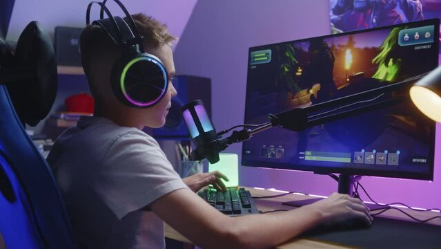 Young gamer in headphones talks with teammates and plays in third person shooter on computer at home. Online video game live streaming or esports competition. Concept of multiplayer PvP on home PC.