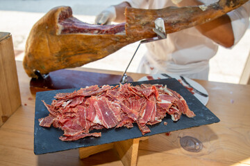 Knife cutting serrano man hand slicing of italian dry cured pork ham