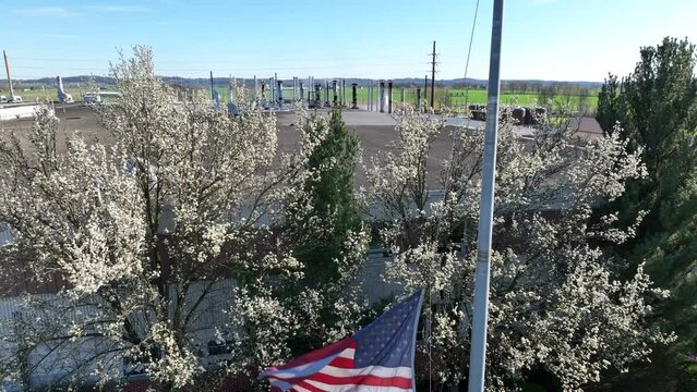 American flag waving in front of industrial building in spring. Rising shot revealing industrial pipes on building roof.
