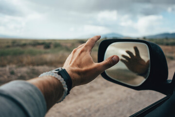 First person perspective of a hand out the window of a moving car