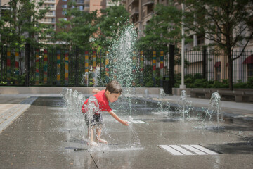 Young boy playing in a fountain at an urban spray park.