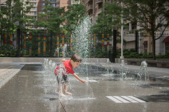 Young boy playing in a fountain at an urban spray park.