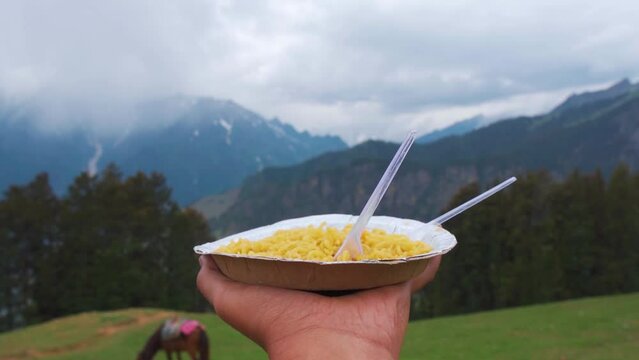 Close up shot of hand holding dish of noodles in background of mountains in Manali, Himachal Pradesh, India. Tourist enjoying Food in mountains during holiday vacation.