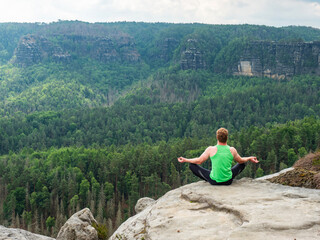 Man sitting on the top of mountain in yoga pose.