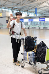 Fototapeta na wymiar The guy with the backpack at the airport. Young handsome man waiting for boarding, walks through airport terminal, Young Asian Korean college student raise v hand to greet