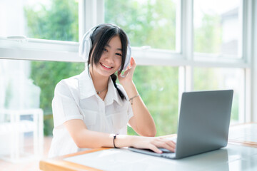 Happy of cute smiles Asian of attractive young Cute girl little wearing headphones and listening music using laptop computer working from at the cafe.Online education, elearning concept.