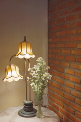 The old vintage table lamp with daisies in glass vase on round table covered with lace tablecloth...
