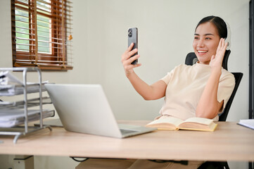 A woman having a video call with her friends on smartphone while sitting at her desk.