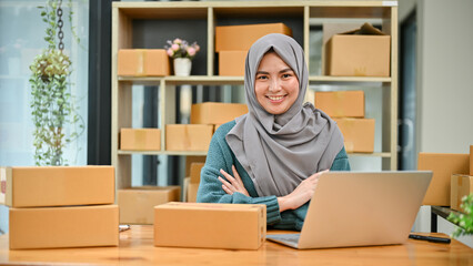 A portrait of a successful young Asian Muslim female online seller sits at her working desk