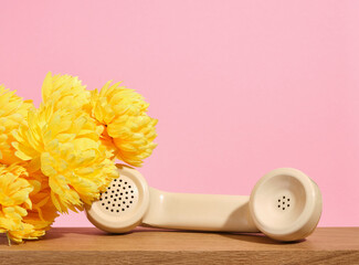 Beige retro telephone handset and yellow lush flowers on a pink background. Copy space for text.