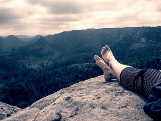 Crossed female barefoot legs of man relax on mountain summit. Hiker lay down and have a rest 