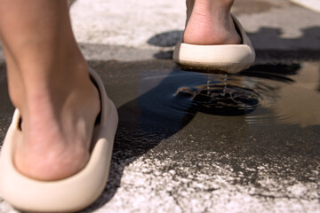 close-up on the legs in brown slippers, female legs cross the puddle on the street close-up on the