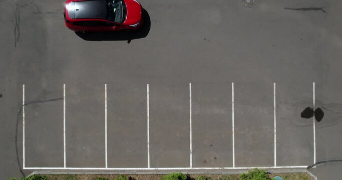 Aerial view of a red car pulling into a parking space. Empty parking lot. Smooth white markings in the parking lot. The car is parked, top view