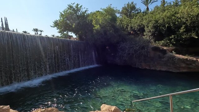 The waterfall in the Garden of Three Nature Reserve and National Park in the Valley of the Springs in Israel. Clear turquoise water against a background of trees