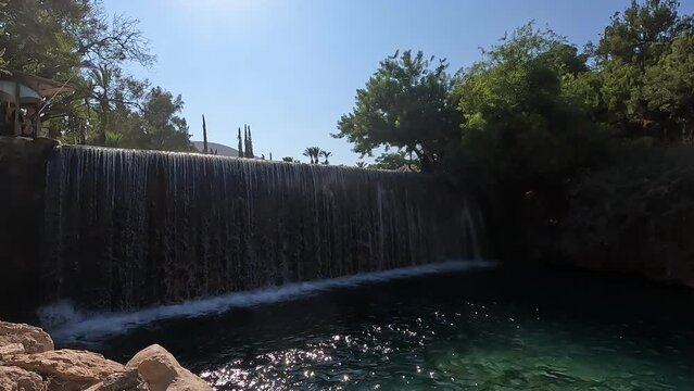 The famous waterfall in the Garden of Three Nature Reserve and National Park in the Valley of the Springs in Israel. Clear turquoise water against a background of trees