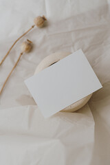 Flat lay blank card sheet, dried poppy stem, clay jar on white crumpled cloth. Top view aesthetic mock up with empty free copy space