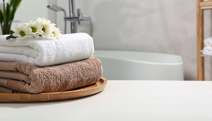 Wooden tray with stacked bath towels and beautiful flowers on white table in bathroom. Space for...