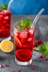 Iced red lemonade drink with fresh mint, sugar syrup and pomegranate juice in glass on a dark concrete background. Refreshing summer drink. Copy space.