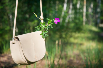 In the summer afternoon in the forest in a woman's bag is a pink flower.