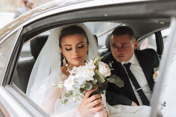 A modern bride and groom in a lace dress in a car window. Beautiful and smiling newlyweds. Happy...