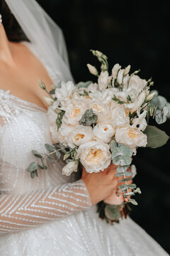Wedding portrait. A brunette bride in a long dress holds her bouquet of roses, peonies and greenery. Cropped photo. Open bust