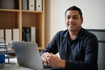 Portrait of cheerful entrepreneur working on laptop at office desk